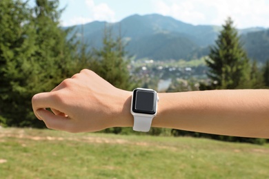 Photo of Woman wearing smart watch with blank screen outdoors, closeup