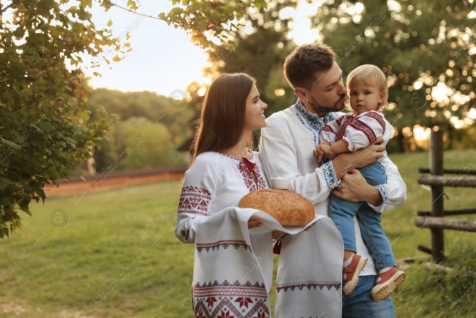 Photo of Happy cute family in embroidered Ukrainian shirts with korovai bread on sunny day. Space for text