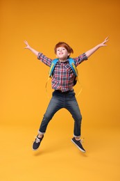 Photo of Happy schoolboy with backpack jumping on orange background