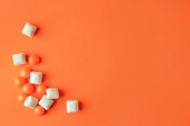 Photo of Different tasty chewing gums on orange background, flat lay. Space for text
