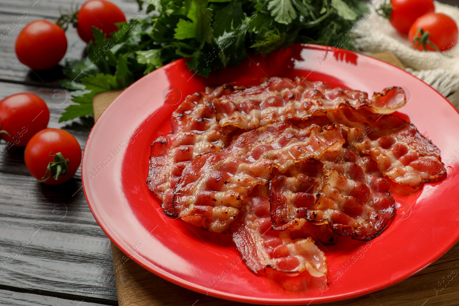 Photo of Plate with fried bacon slices, tomatoes and parsley on wooden table, closeup