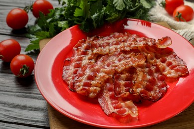 Plate with fried bacon slices, tomatoes and parsley on wooden table, closeup