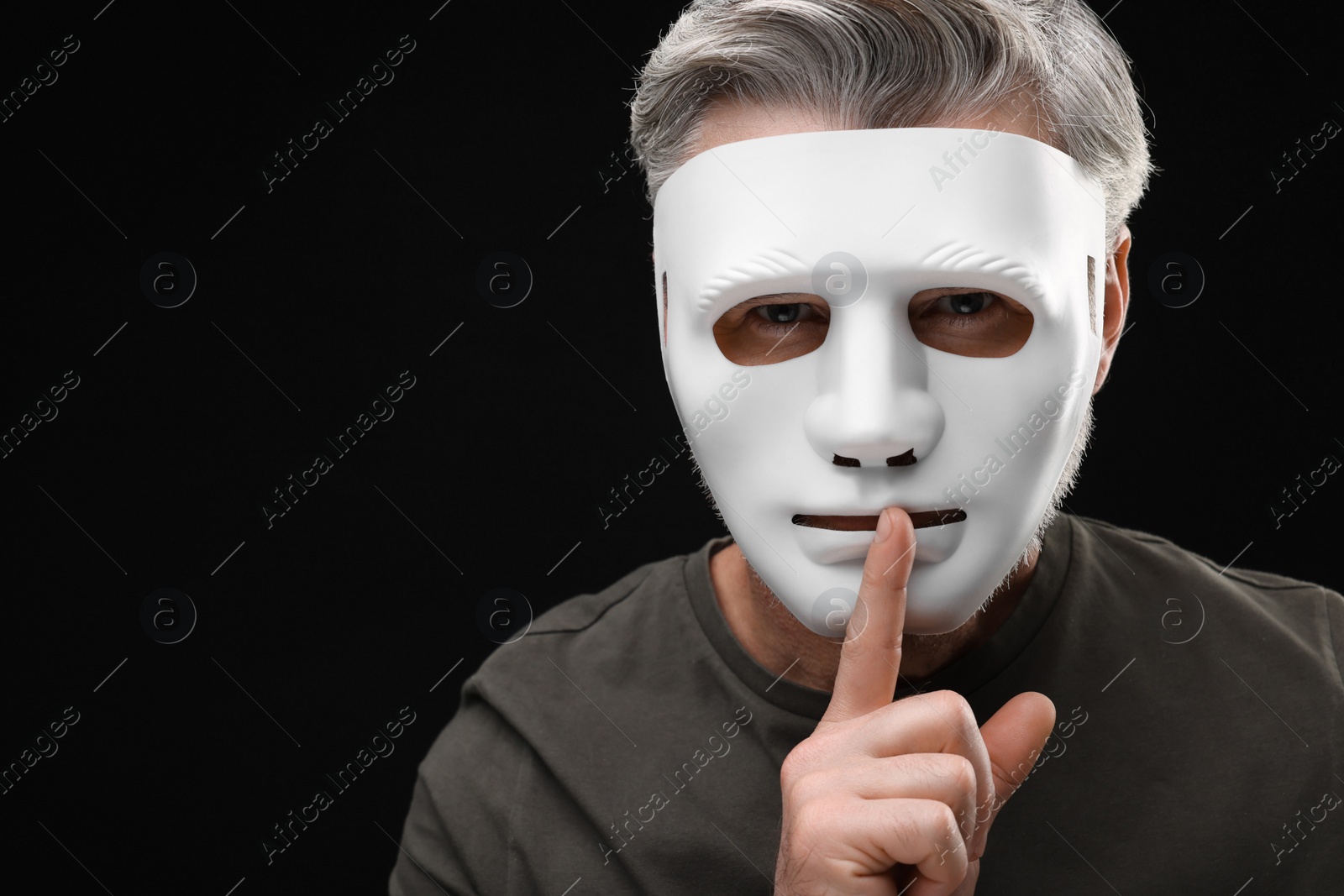 Photo of Man in mask showing hush gesture against black background. Space for text
