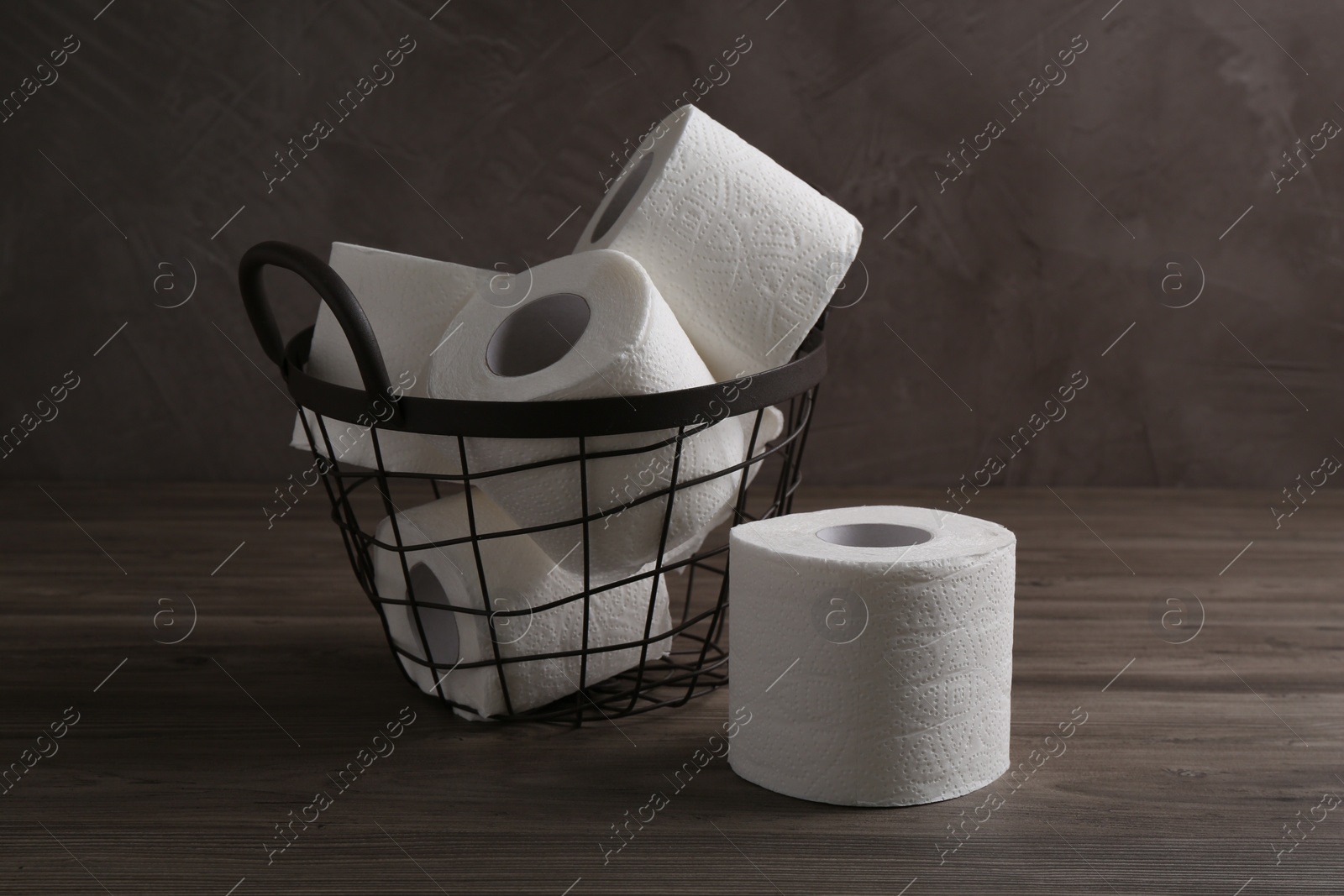 Photo of Soft toilet paper rolls in metal basket on wooden table