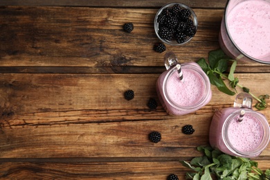 Photo of Tasty fresh milk shakes with blackberries on wooden table, flat lay. Space for text