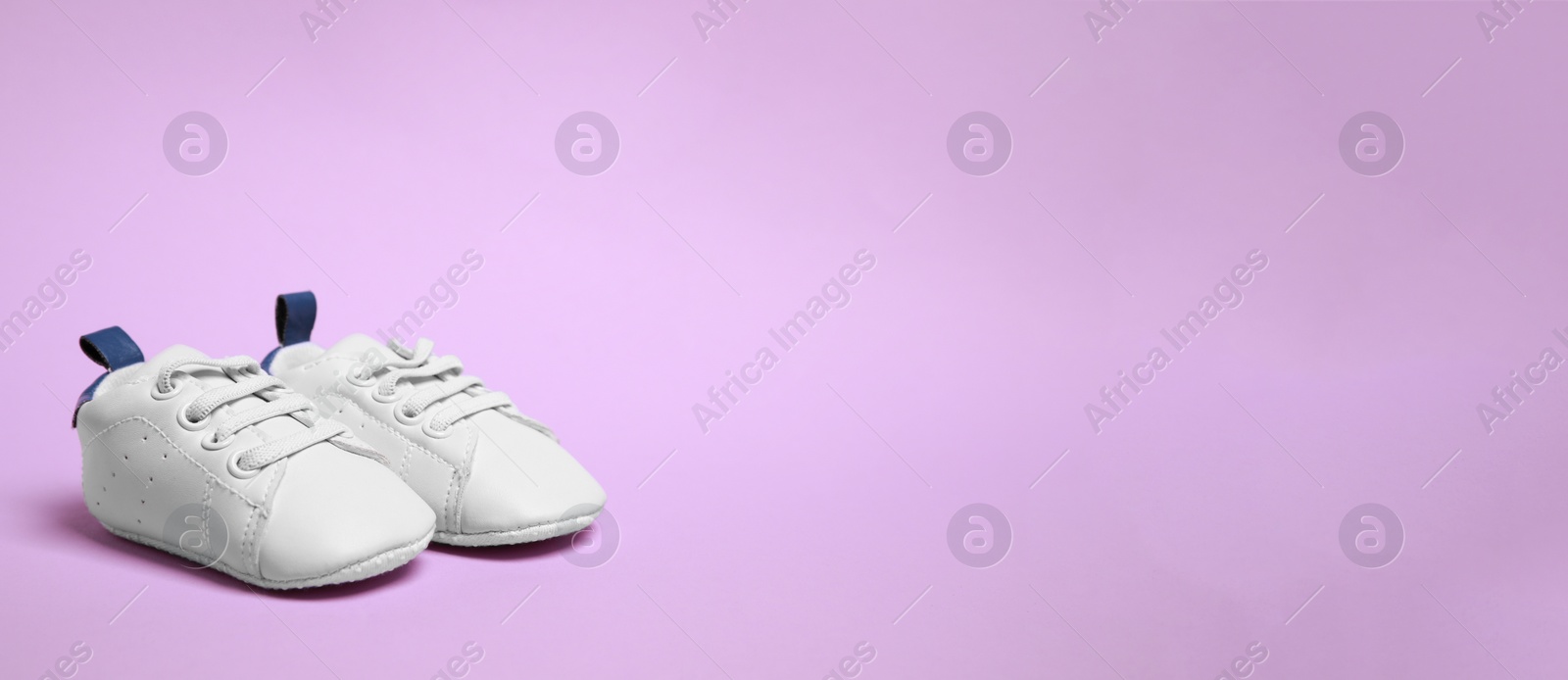 Image of Cute baby shoes on violet background, space for text. Banner design