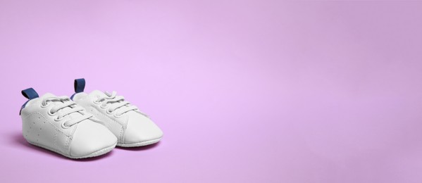 Image of Cute baby shoes on violet background, space for text. Banner design