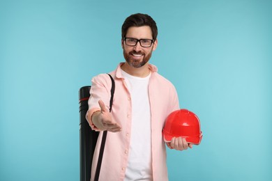 Photo of Architect with drawing tube and hard hat greeting someone on light blue background