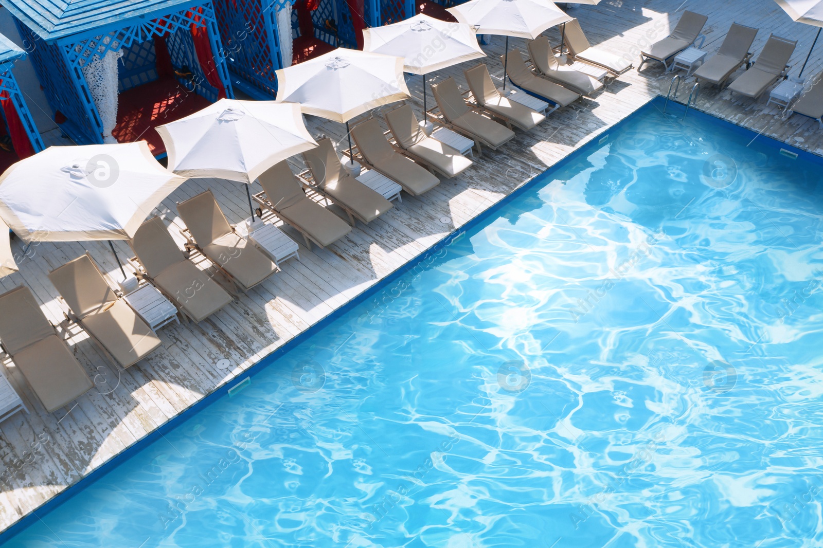 Image of Lounge chairs with umbrellas near swimming pool on sunny day 