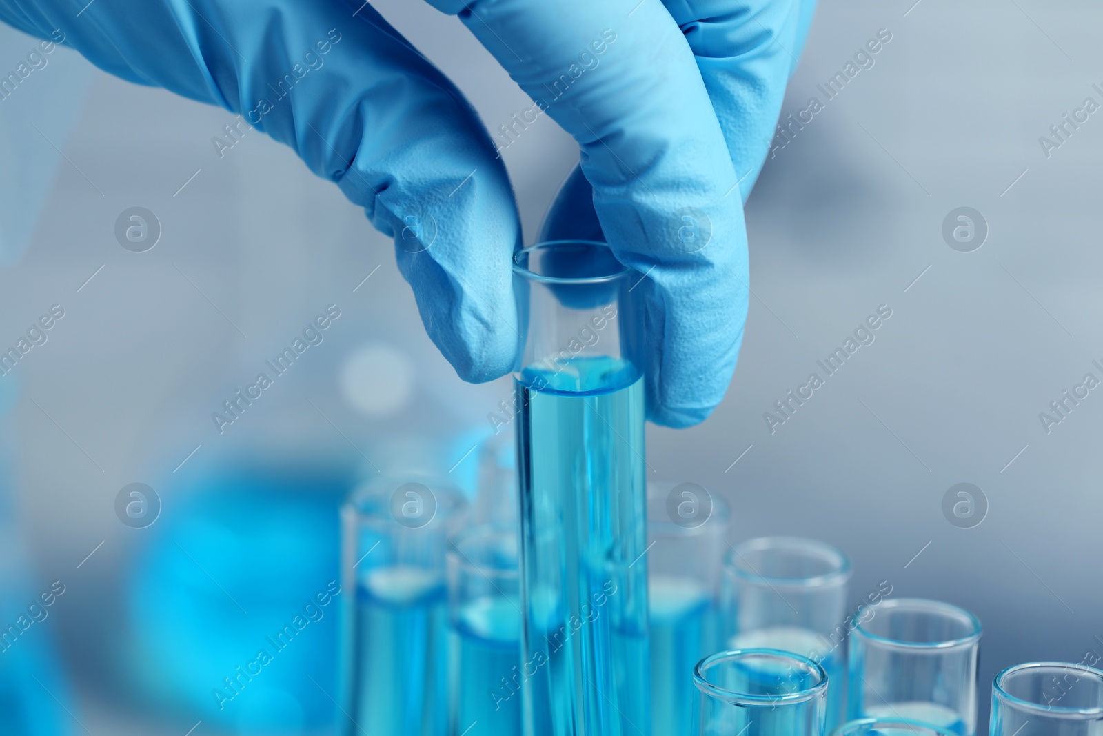 Photo of Scientist taking test tube with light blue liquid on blurred background, closeup