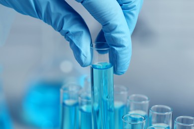 Scientist taking test tube with light blue liquid on blurred background, closeup