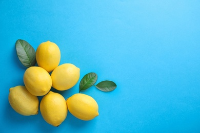 Fresh lemons and leaves on blue background, flat lay. Space for text