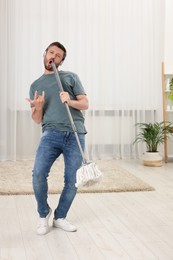 Photo of Happy man in headphones with mop singing while cleaning at home