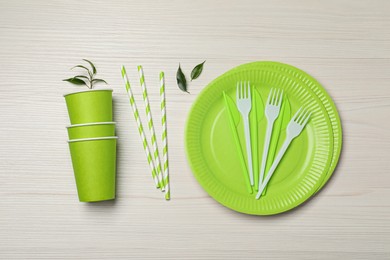 Photo of Flat lay composition with disposable tableware and green leaves on white wooden background