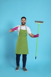 Young man with green broom on light blue background