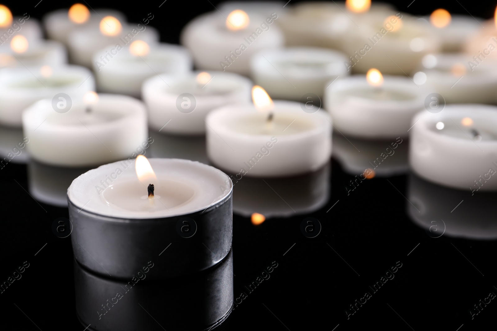 Photo of Wax candles burning on table in darkness, closeup