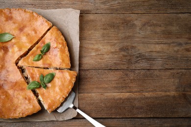 Photo of Delicious pie with meat and basil on wooden table, top view. Space for text