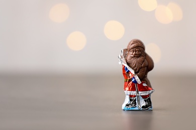 Photo of Chocolate Santa Claus candy in slightly open foil wrapper on light background, space for text