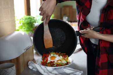 Photo of Woman putting freshly fried eggs with vegetables onto plate in kitchen, closeup