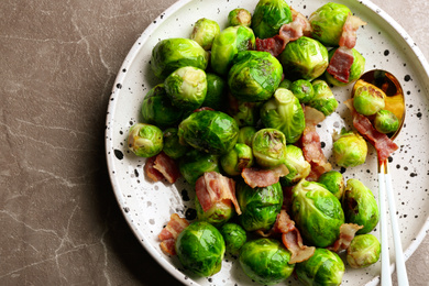 Photo of Delicious Brussels sprouts with bacon on marble table, top view