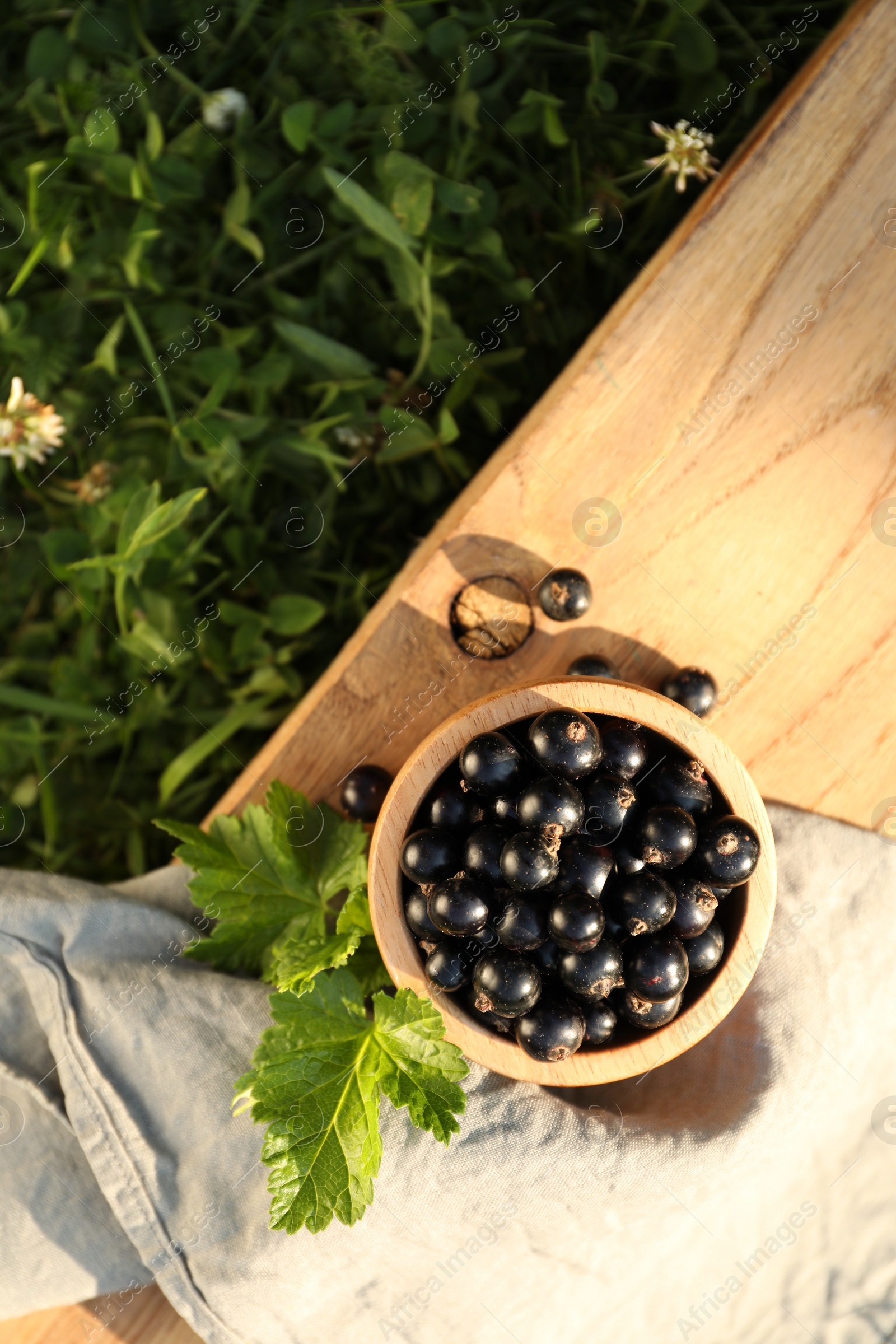 Photo of Ripe blackcurrants in bowl and leaves on wooden table outdoors, top view. Space for text