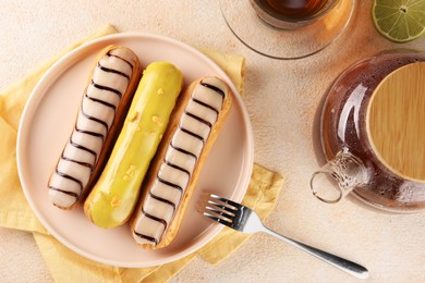 Different tasty glazed eclairs and tea served on color textured table, flat lay