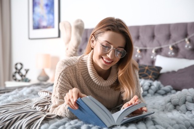 Photo of Young woman reading book on bed at home