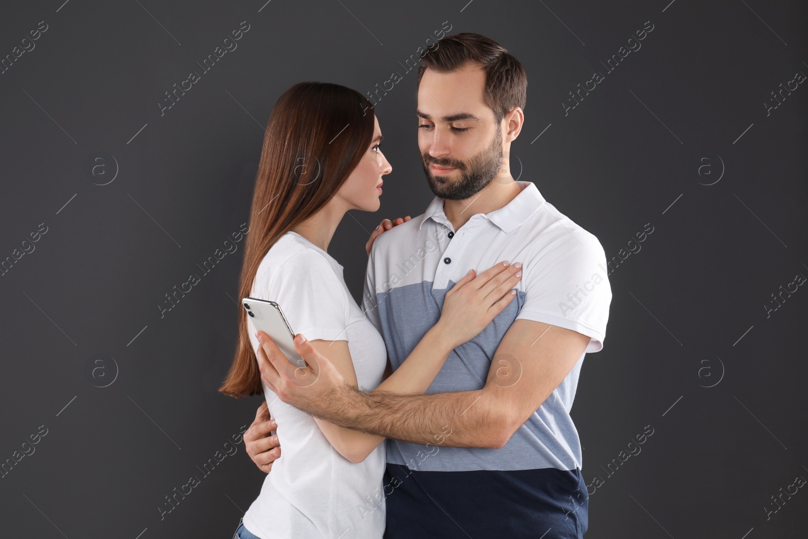 Photo of Man interested in smartphone while hugging his girlfriend on black background. Relationship problems