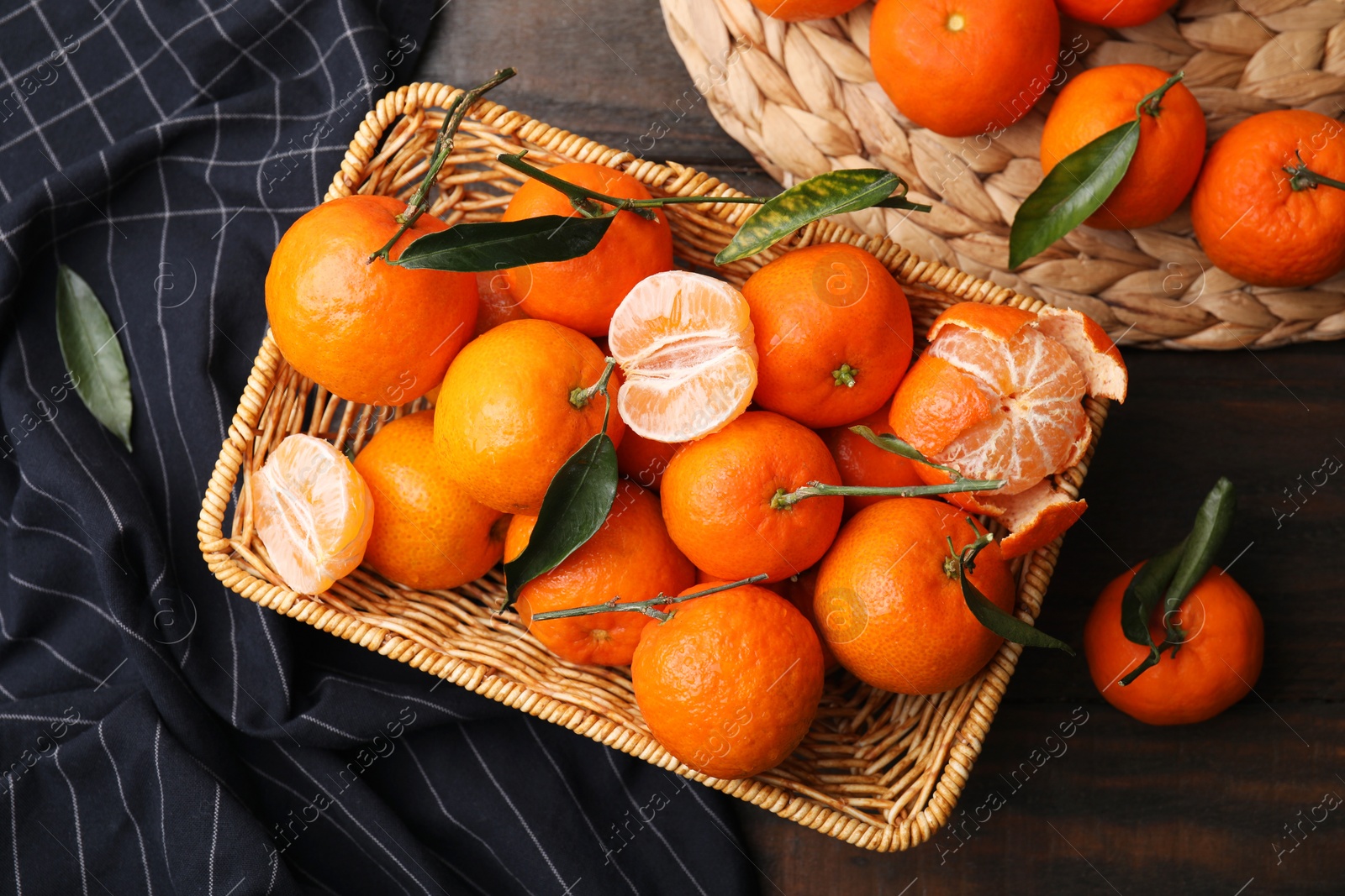 Photo of Fresh ripe tangerines with green leaves in wicker basket on wooden table, flat lay
