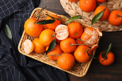 Fresh ripe tangerines with green leaves in wicker basket on wooden table, flat lay