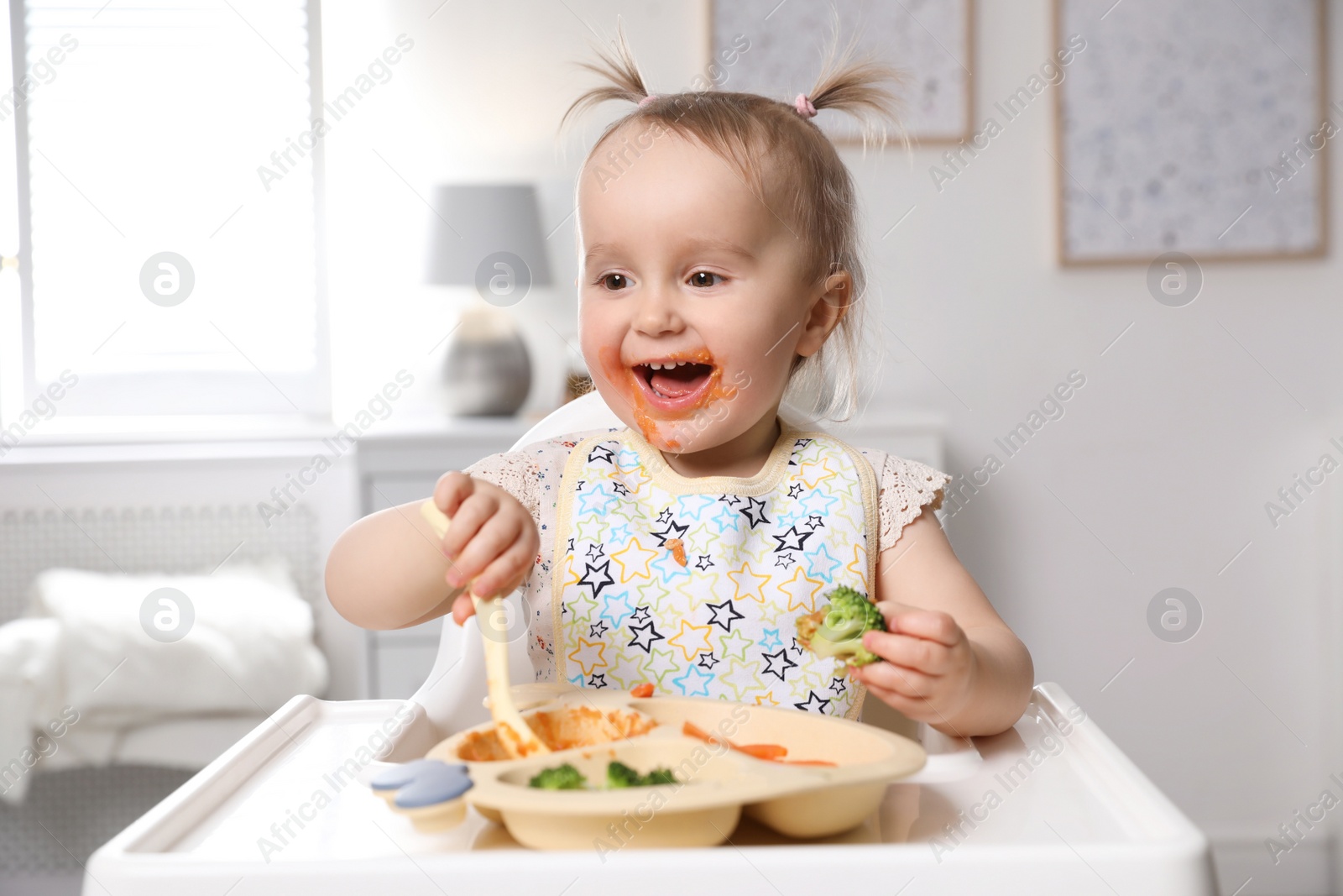 Photo of Cute little baby eating food in high chair at home