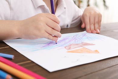 Photo of Little boy drawing ship with pencil at wooden table indoors, closeup. Child`s art