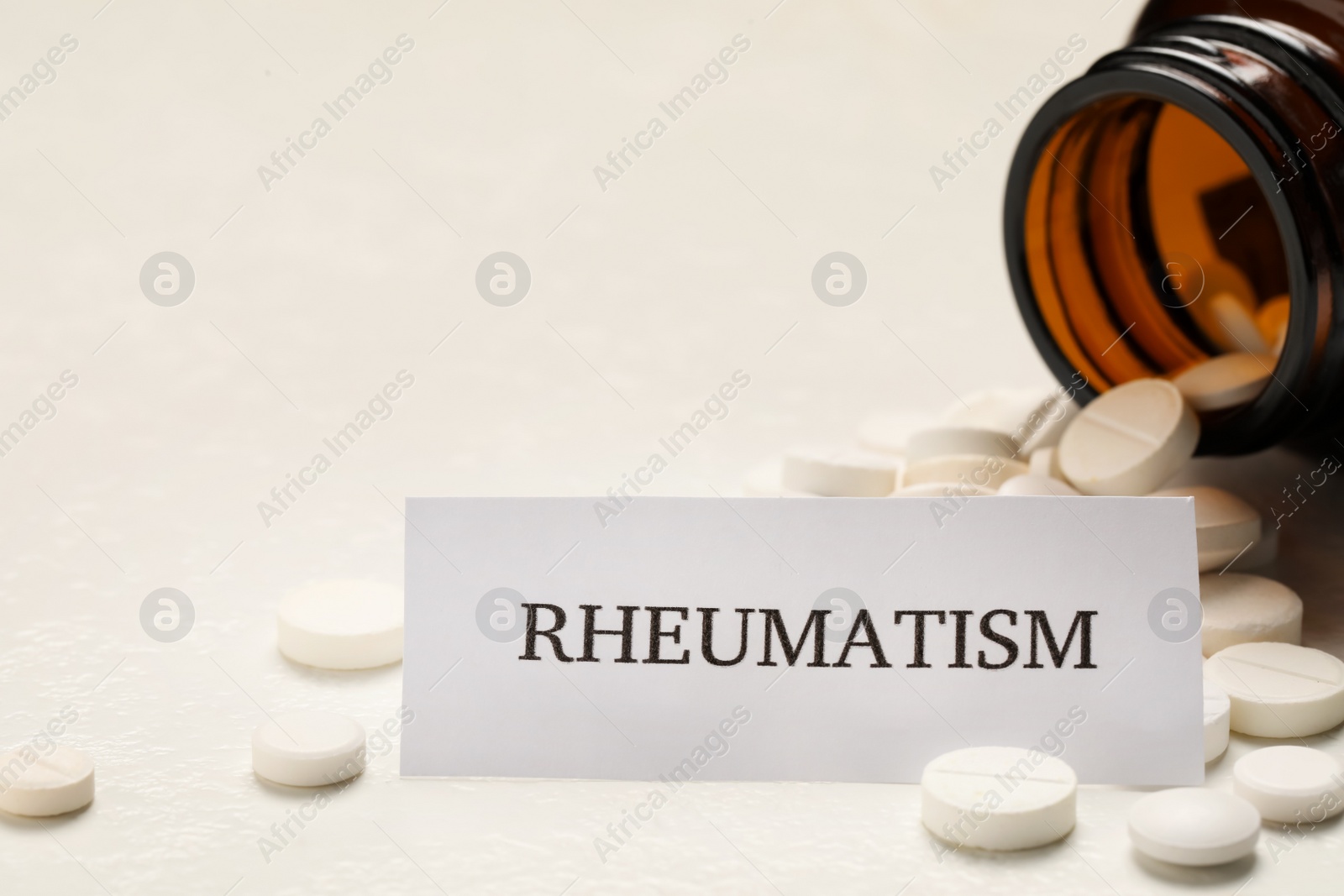 Photo of Card with word Rheumatism and pills on white table, closeup