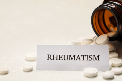 Photo of Card with word Rheumatism and pills on white table, closeup