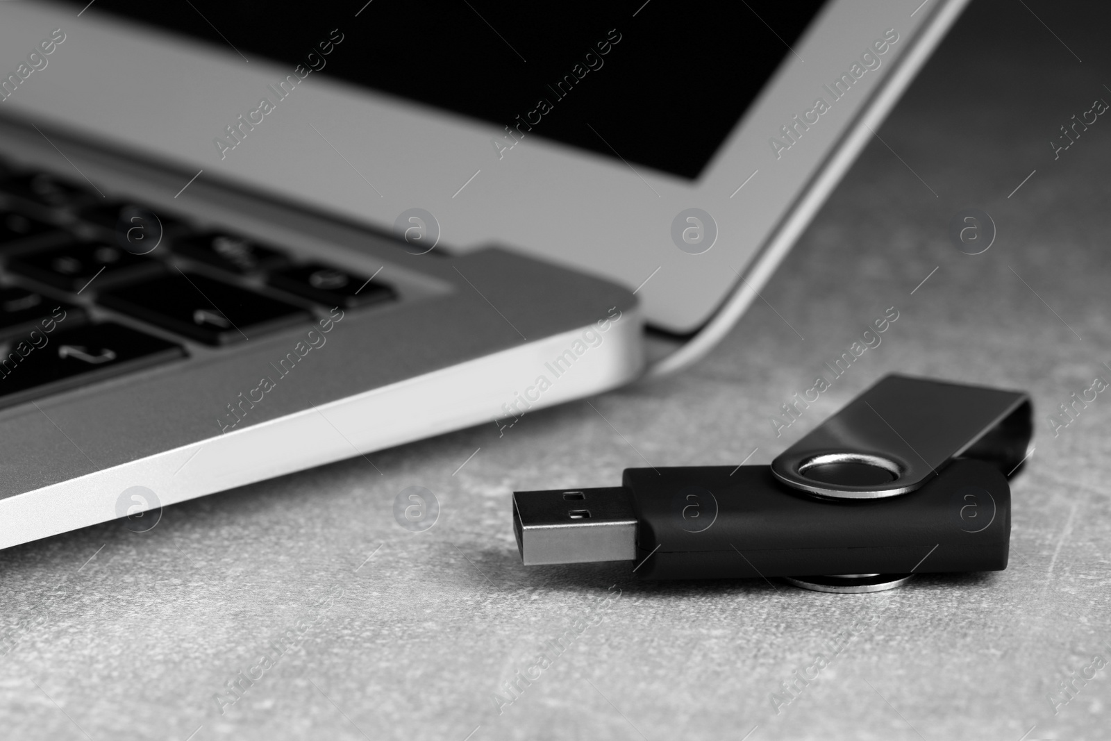 Photo of Usb flash drive and laptop on grey table, closeup