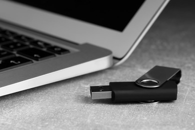 Usb flash drive and laptop on grey table, closeup
