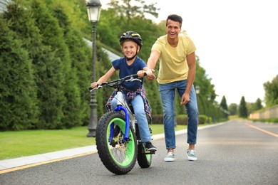 Image of Dad teaching son to ride bicycle outdoors