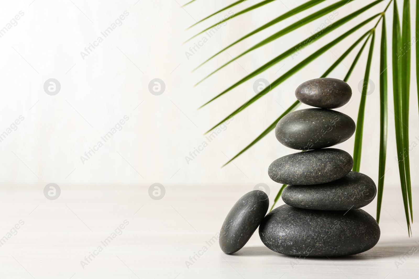 Photo of Stack of spa stones and palm leaf on table against white background, space for text