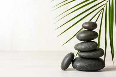 Photo of Stack of spa stones and palm leaf on table against white background, space for text