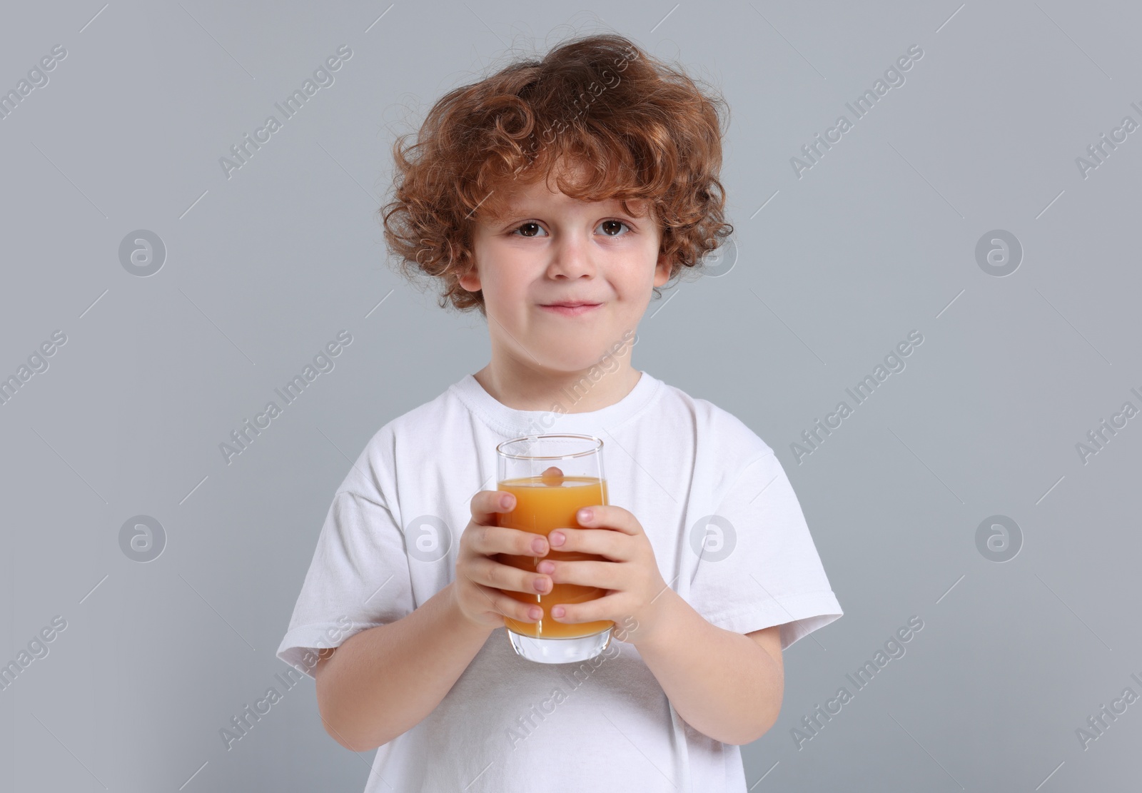 Photo of Cute little boy with glass of fresh juice on light gray background