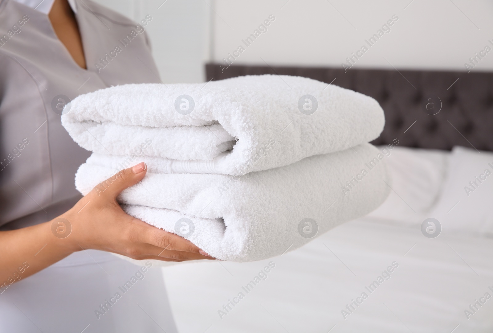 Photo of Young chambermaid with clean towels in bedroom, closeup
