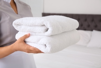Photo of Young chambermaid with clean towels in bedroom, closeup