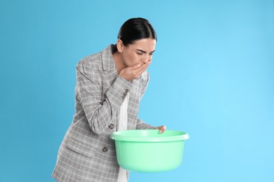 Photo of Woman with basin suffering from nausea on light blue background, space for text. Food poisoning