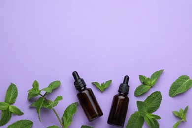 Photo of Bottles of essential oil and mint on violet background, flat lay. Space for text
