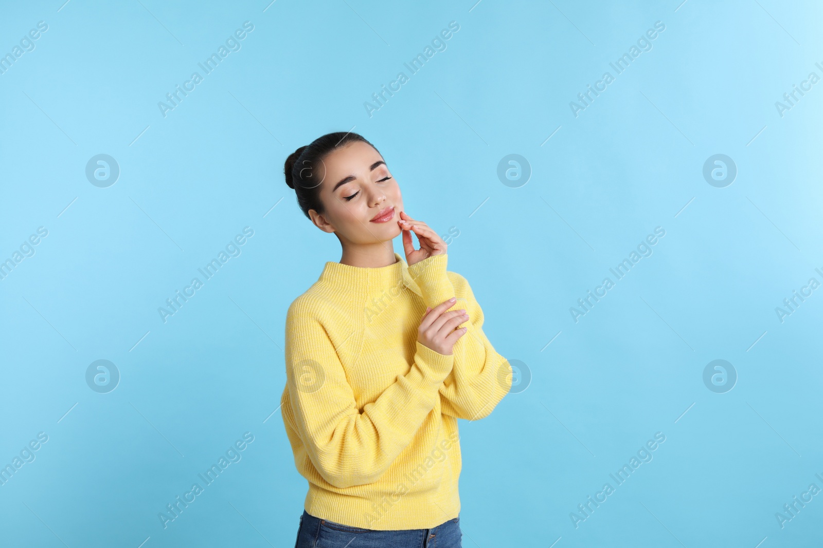 Photo of Beautiful young woman wearing yellow warm sweater on light blue background