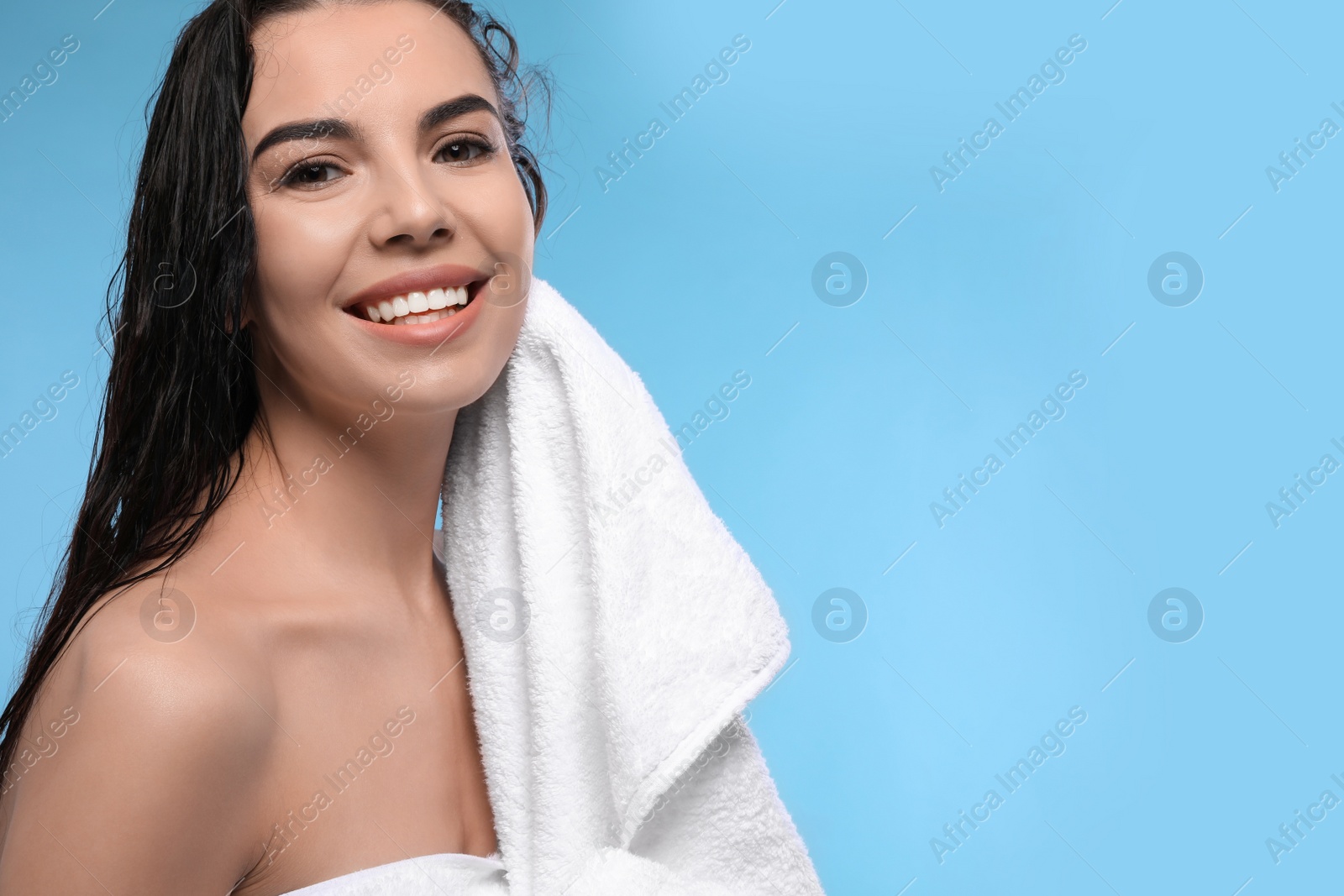 Photo of Happy young woman drying hair with towel after washing on light blue background. Space for text