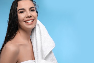 Happy young woman drying hair with towel after washing on light blue background. Space for text