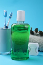 Photo of Fresh mouthwash in bottle, dental floss and toothbrushes on light blue background, closeup