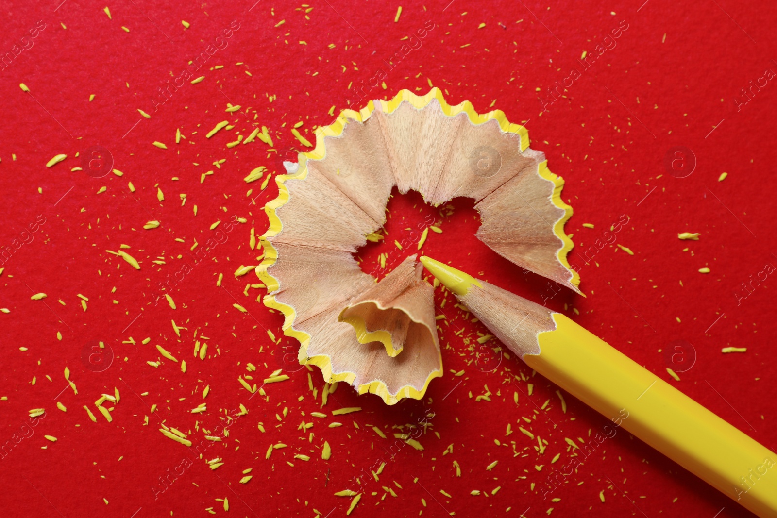 Photo of Yellow pencil and wooden shaving on red background, flat lay