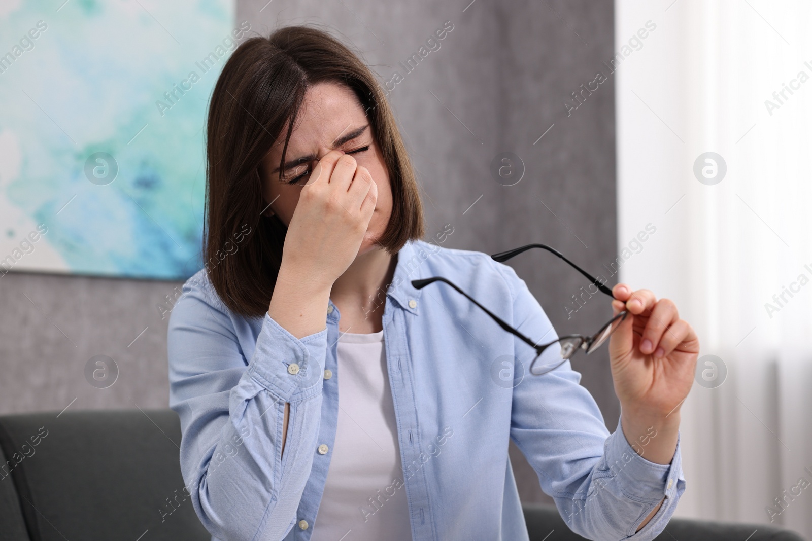 Photo of Overwhelmed woman with glasses sitting on sofa indoors